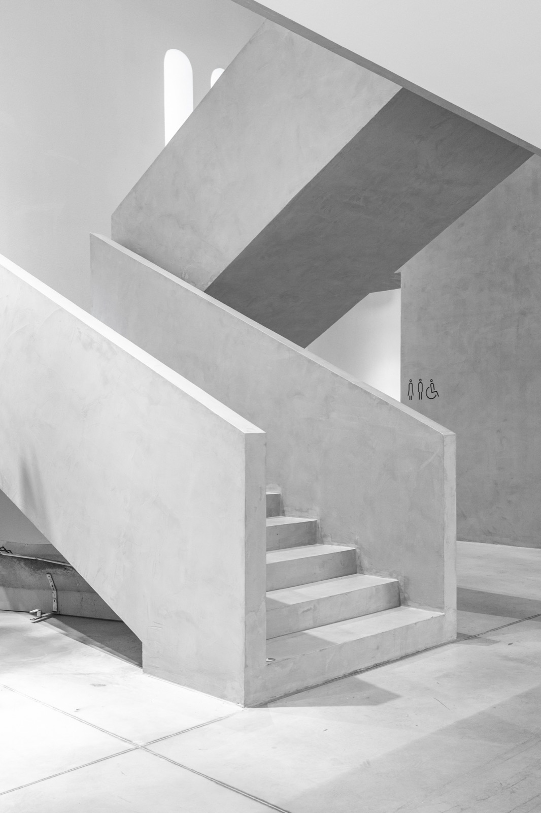 Architektonické schodiště z betonové stěrky, hladké šedé stěny galerie — realizace Dehner
