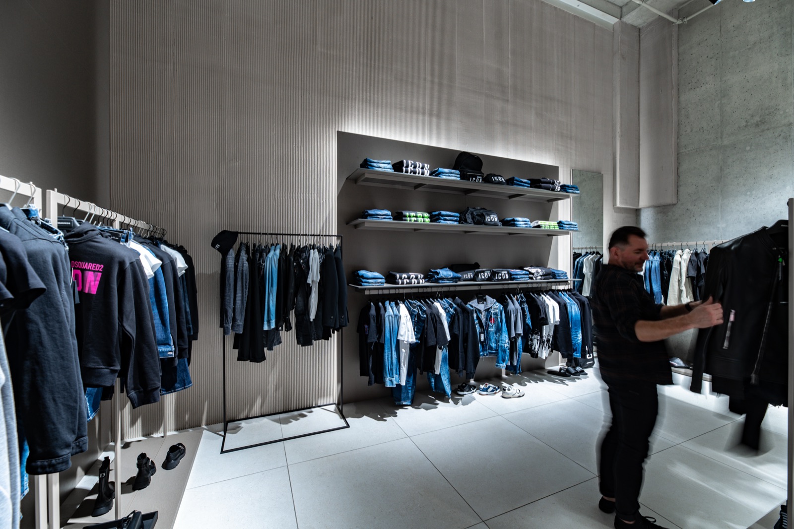 Butik se žebrovanou stěrkou na stěně, zákazník prohlíží oblečení — realizace Dehner